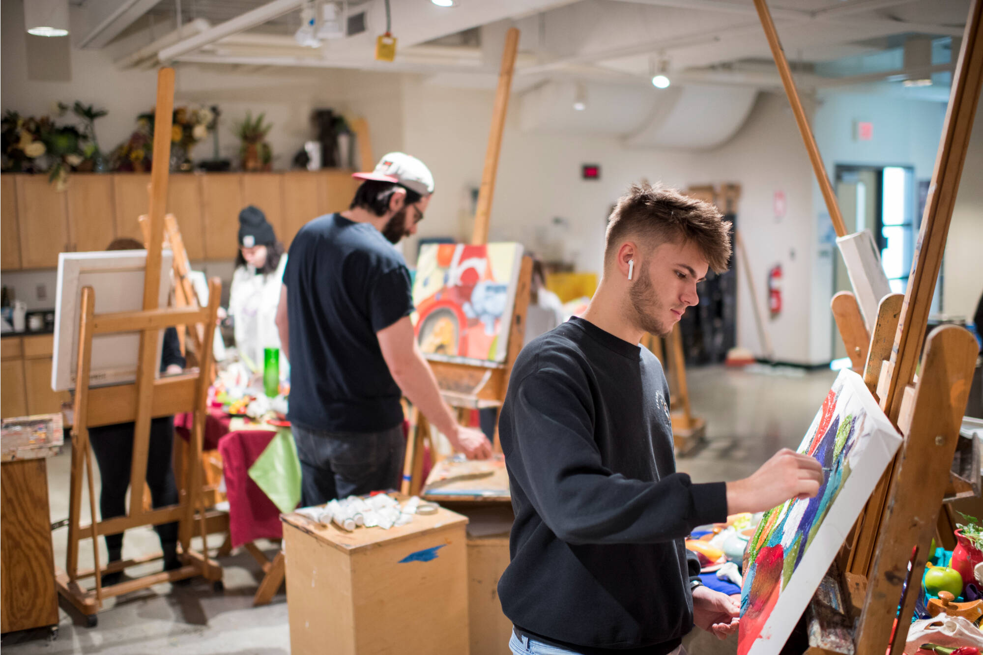 Students work on their individual paintings on easels.